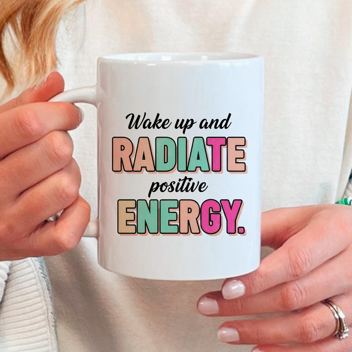 White ceramic mug held in hands, “Wake up and RADIATE positive ENERGY” print