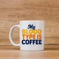 White ceramic coffee mug with handle, text “My BLOOD TYPE IS COFFEE”.