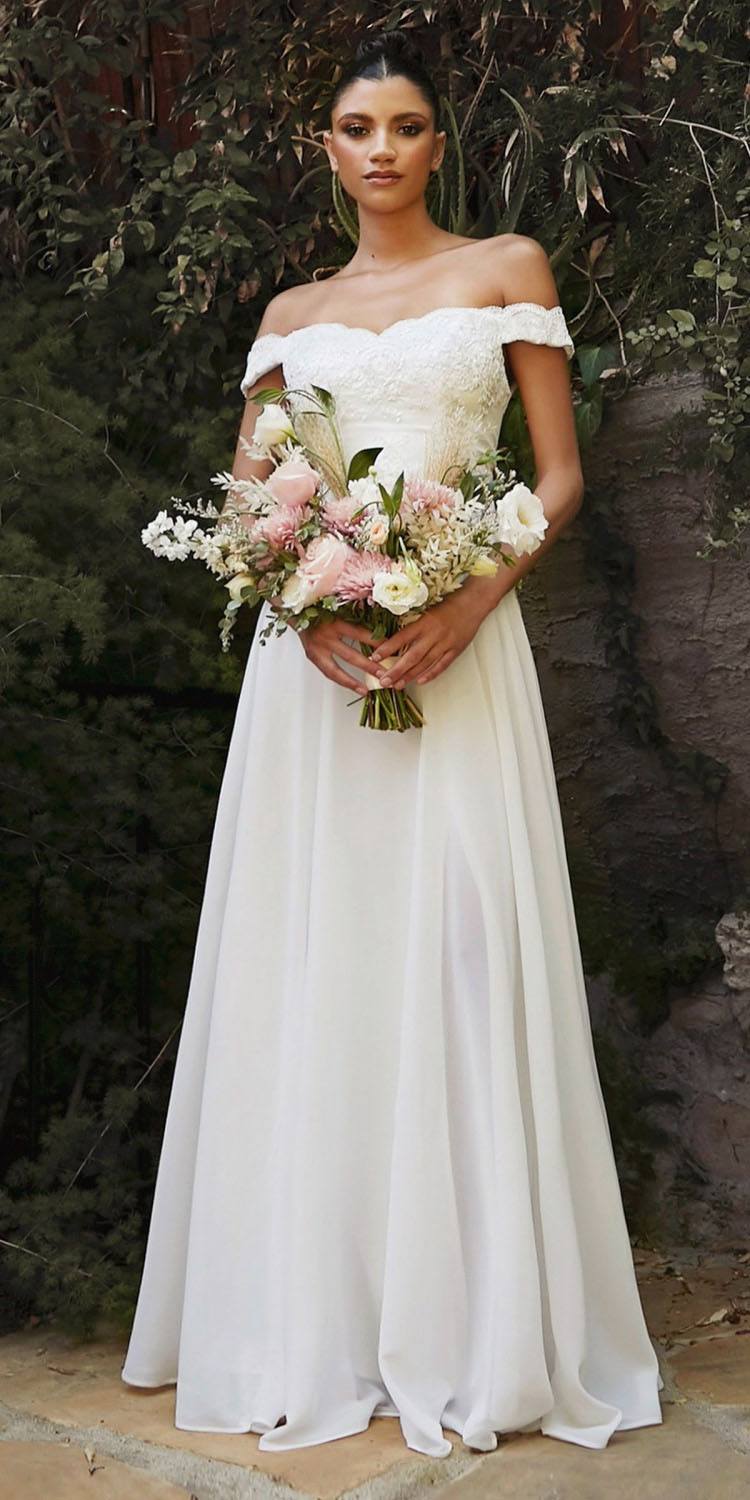 Off-shoulder off-white lace long gown with bouquet held at waist