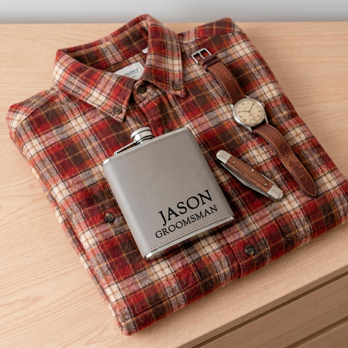 Stainless steel flask with engraved front tag, tucked into plaid button-up shirt