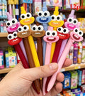 Googly-eyed ink pens with cartoon faces, held in hand; multicolor barrels