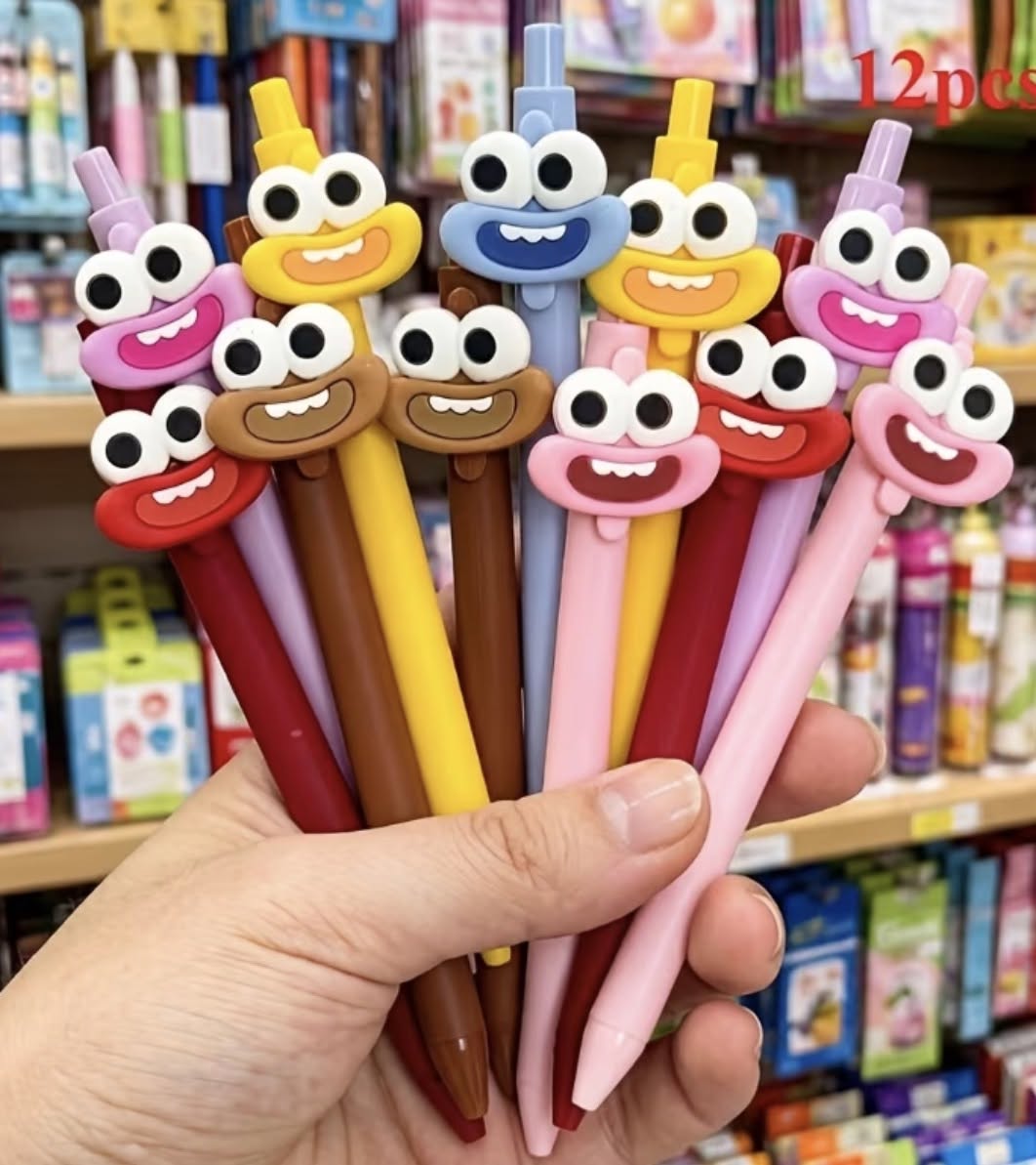 Googly-eyed ink pens with cartoon faces, held in hand; multicolor barrels