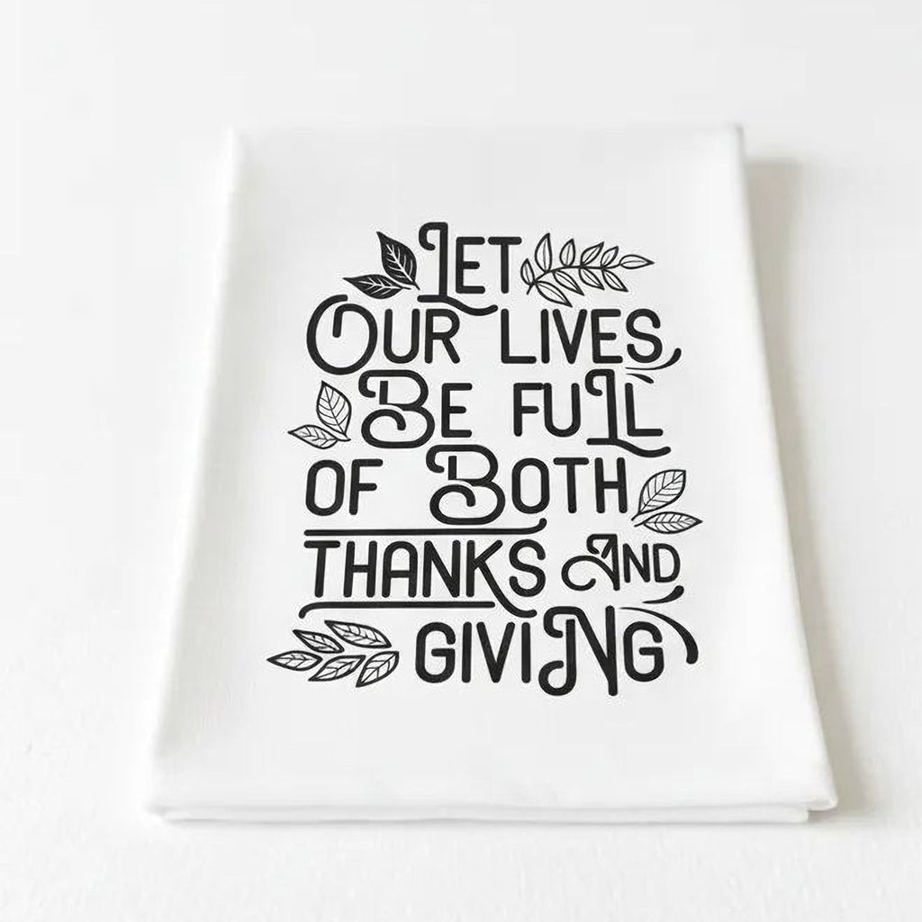 White Thanksgiving kitchen towel folded, featuring black “Let our lives be full of both…”