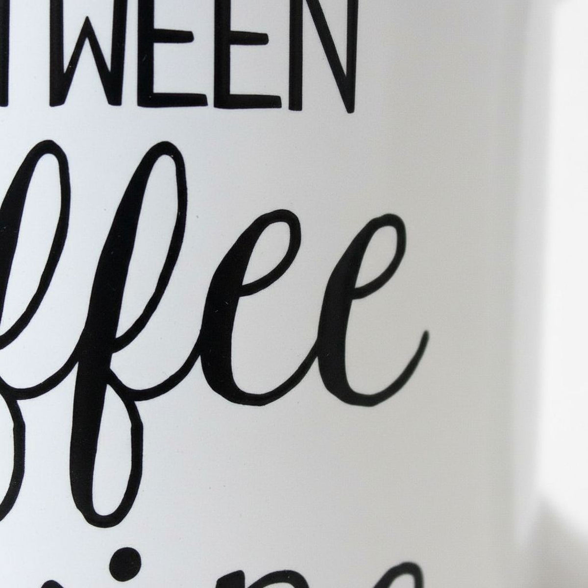 Close-up of white mug print: “Life is what happens between coffee & wine” in black.