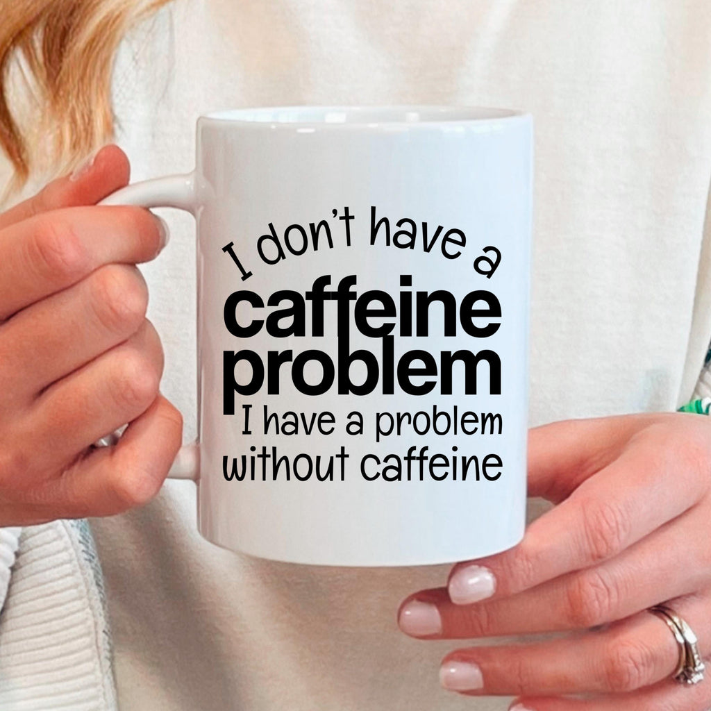 White ceramic mug held in hands, featuring "I don't have a caffeine problem" quote
