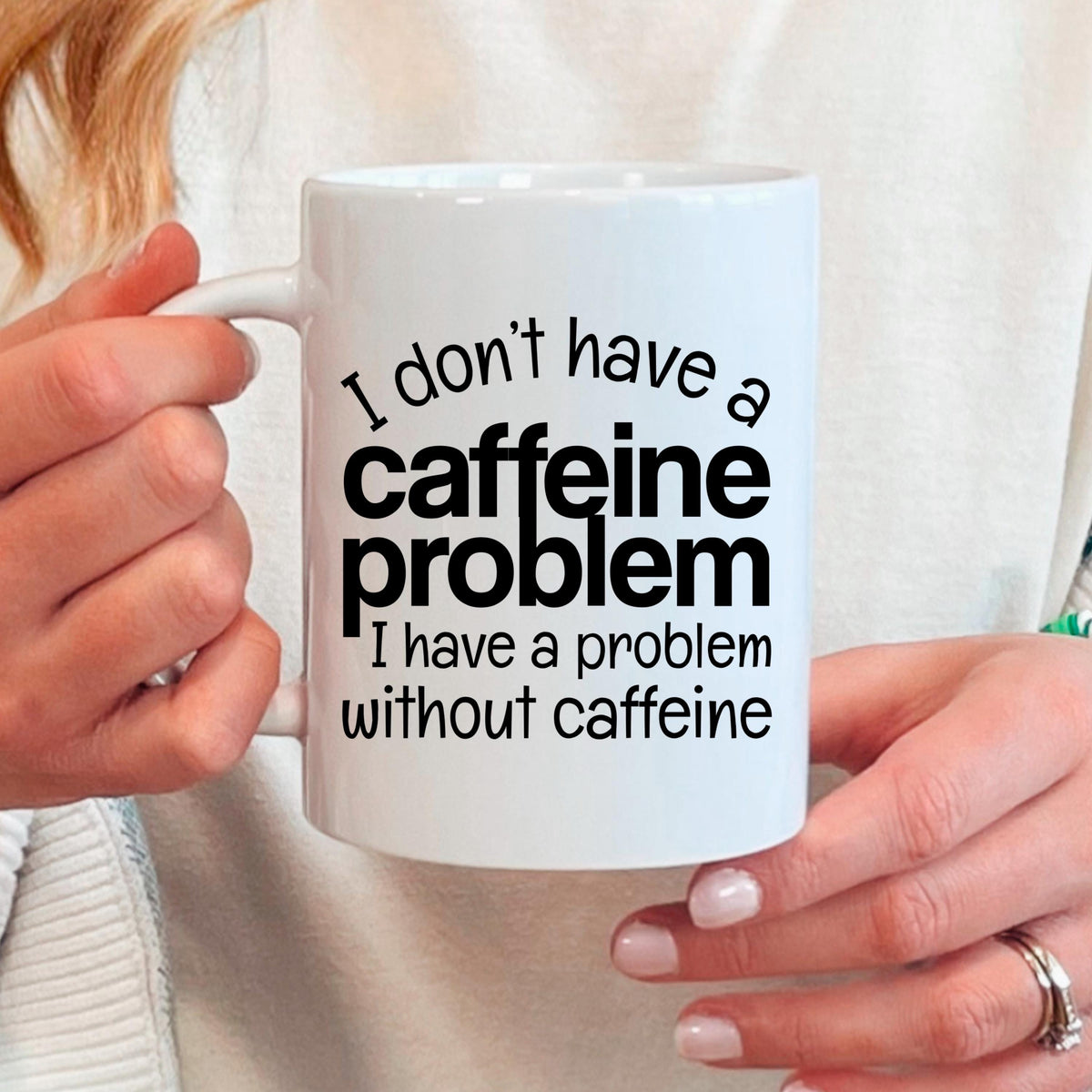 White ceramic mug held in hands, featuring "I don't have a caffeine problem" quote
