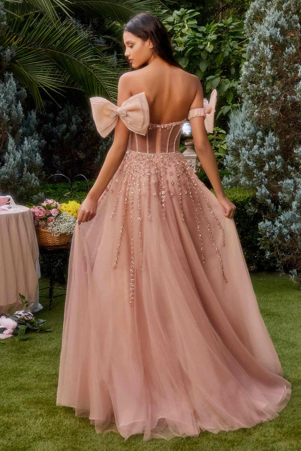 Rose gold strapless beaded gown from back view with bow arm bands and flowing tulle skirt.