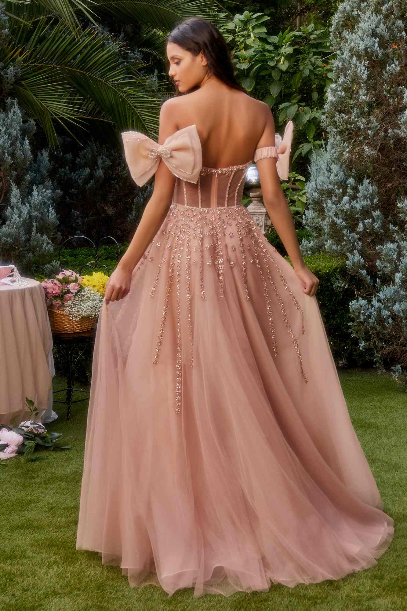 Rose gold strapless beaded gown from back view with bow arm bands and flowing tulle skirt.