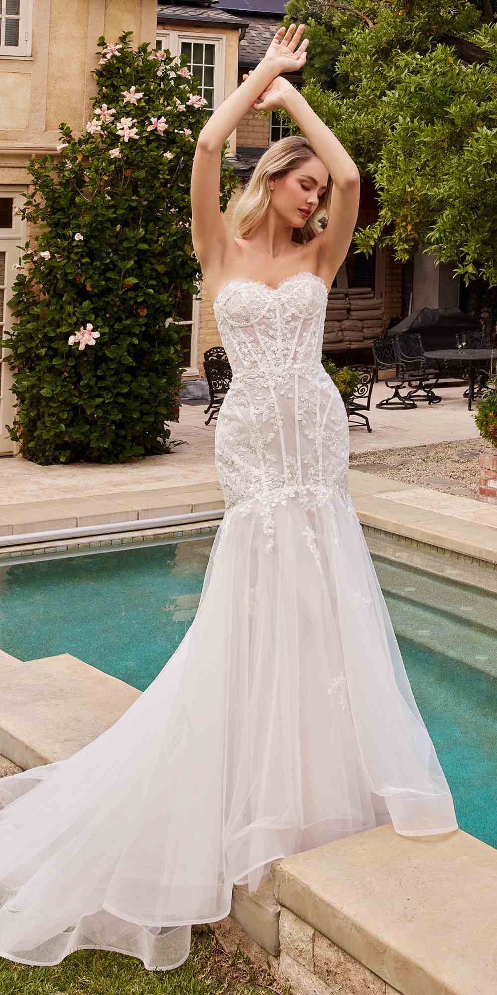 Off-white strapless mermaid dress with lace bodice and flowing tulle skirt, arms raised