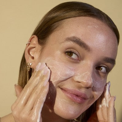 Skincare foam on face with hands applying cleanser, close-up
