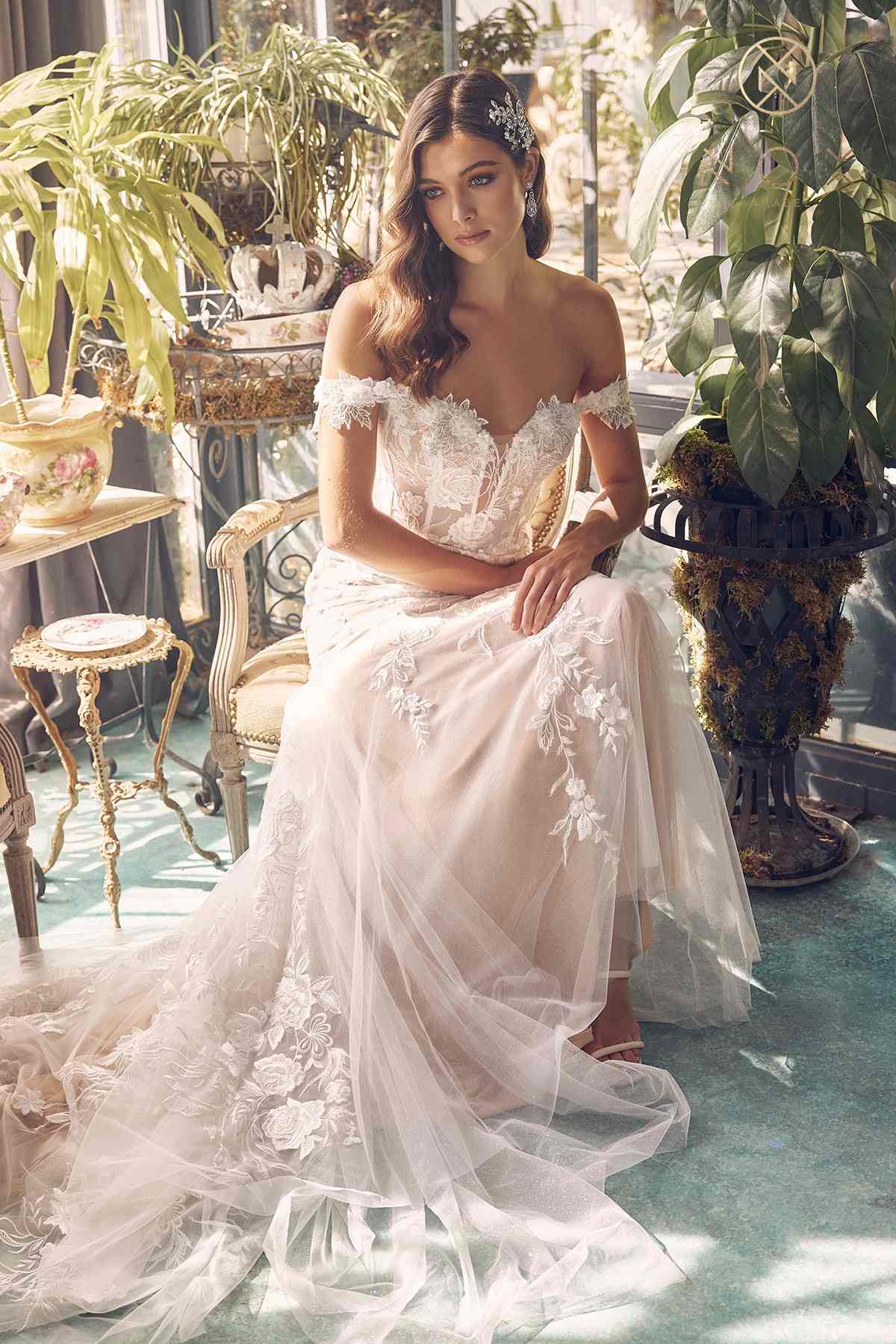 Off-shoulder embroidered wedding gown, fitted bodice and layered tulle skirt, seated pose
