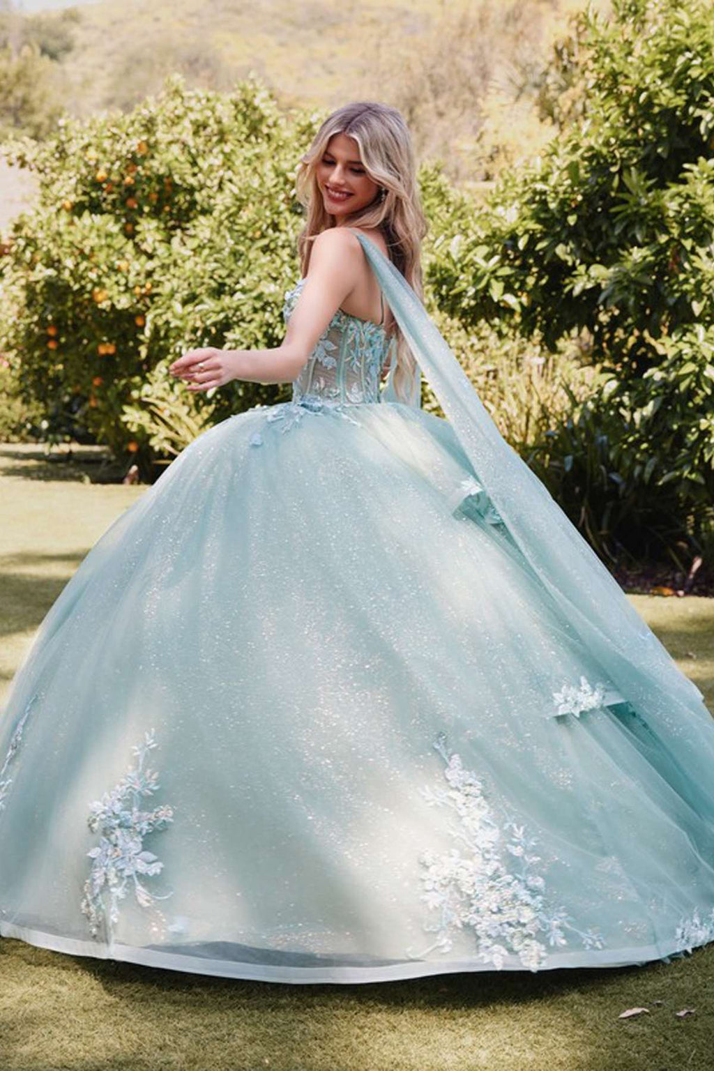 Sage green quinceanera gown with floral appliques, cape sleeves, and voluminous tulle skirt