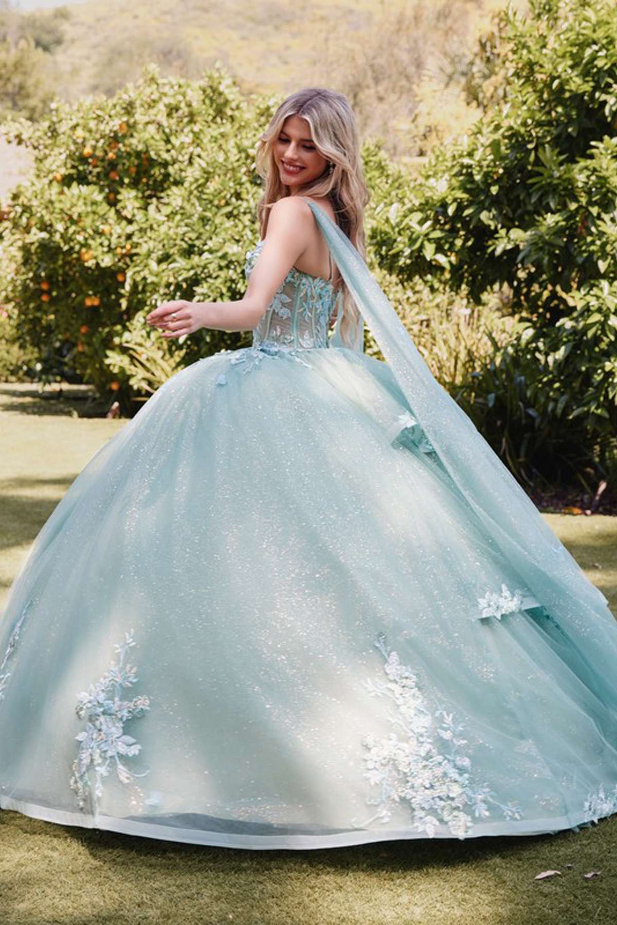 Sage green quinceanera gown with floral appliques, cape sleeves, and voluminous tulle skirt