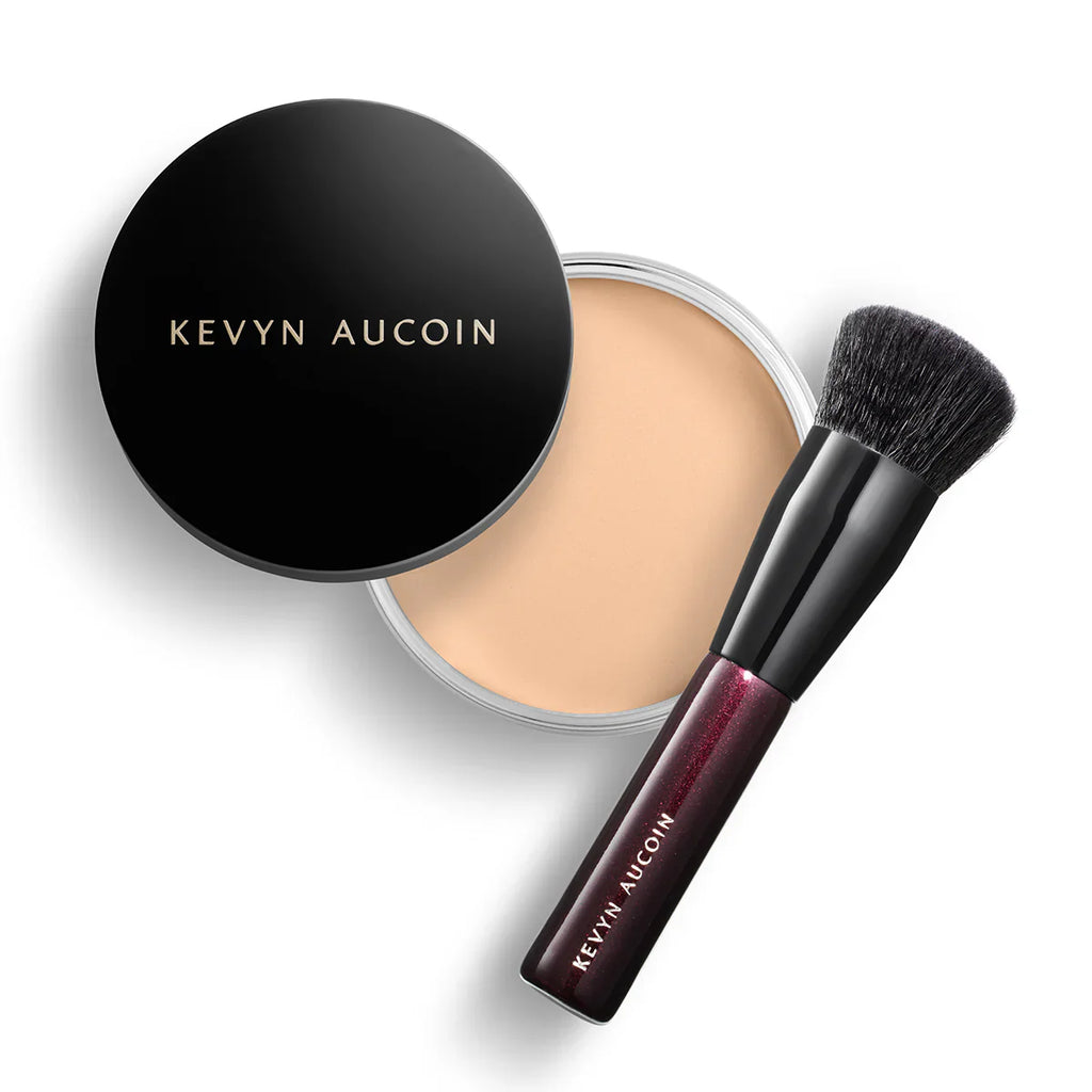 Foundation balm compact with round black lid, light beige balm, and makeup brush