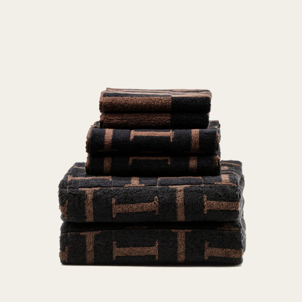 Stack of cotton towels in tobacco and black with woven geometric pattern