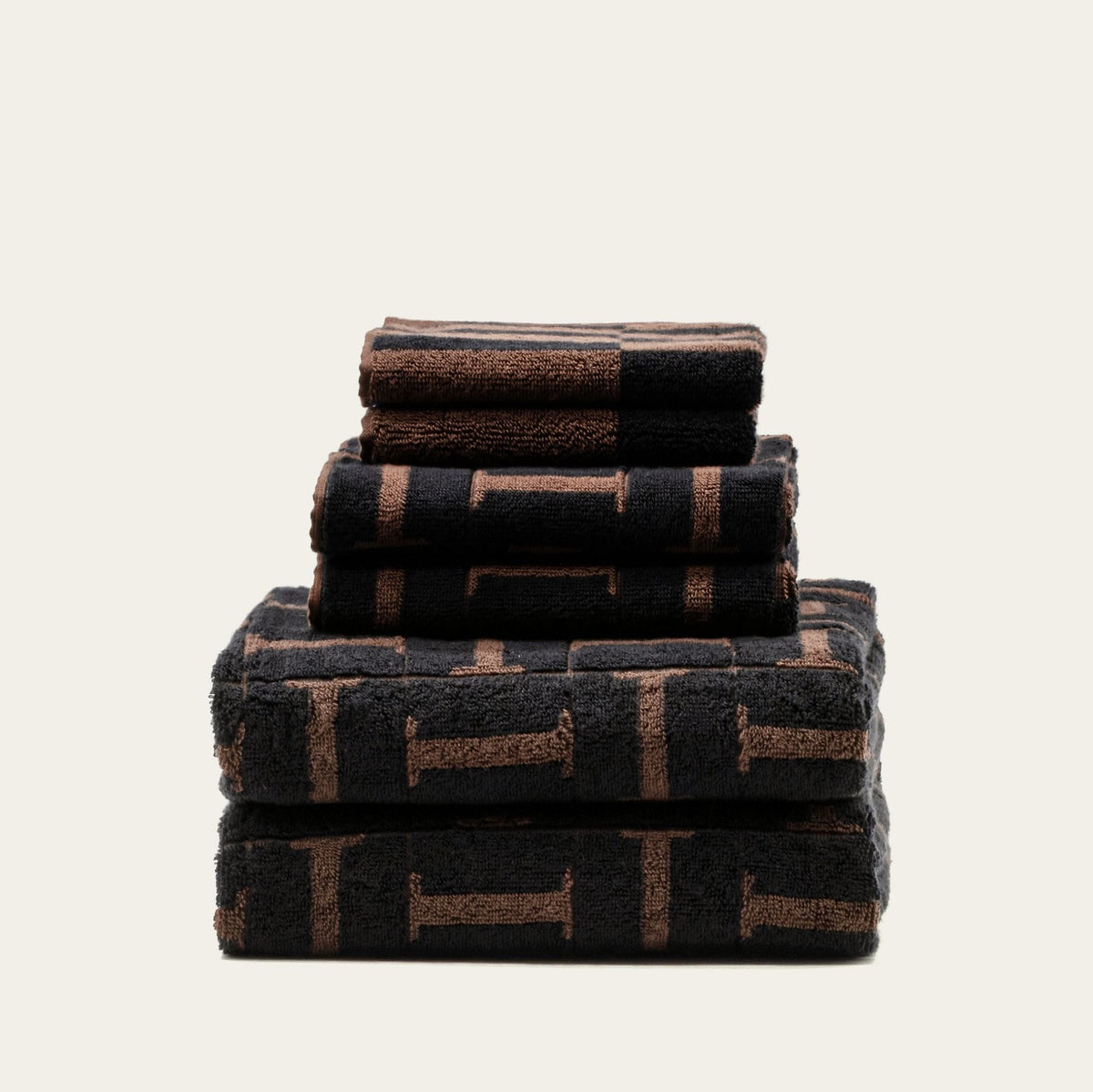 Stack of cotton towels in tobacco and black with woven geometric pattern