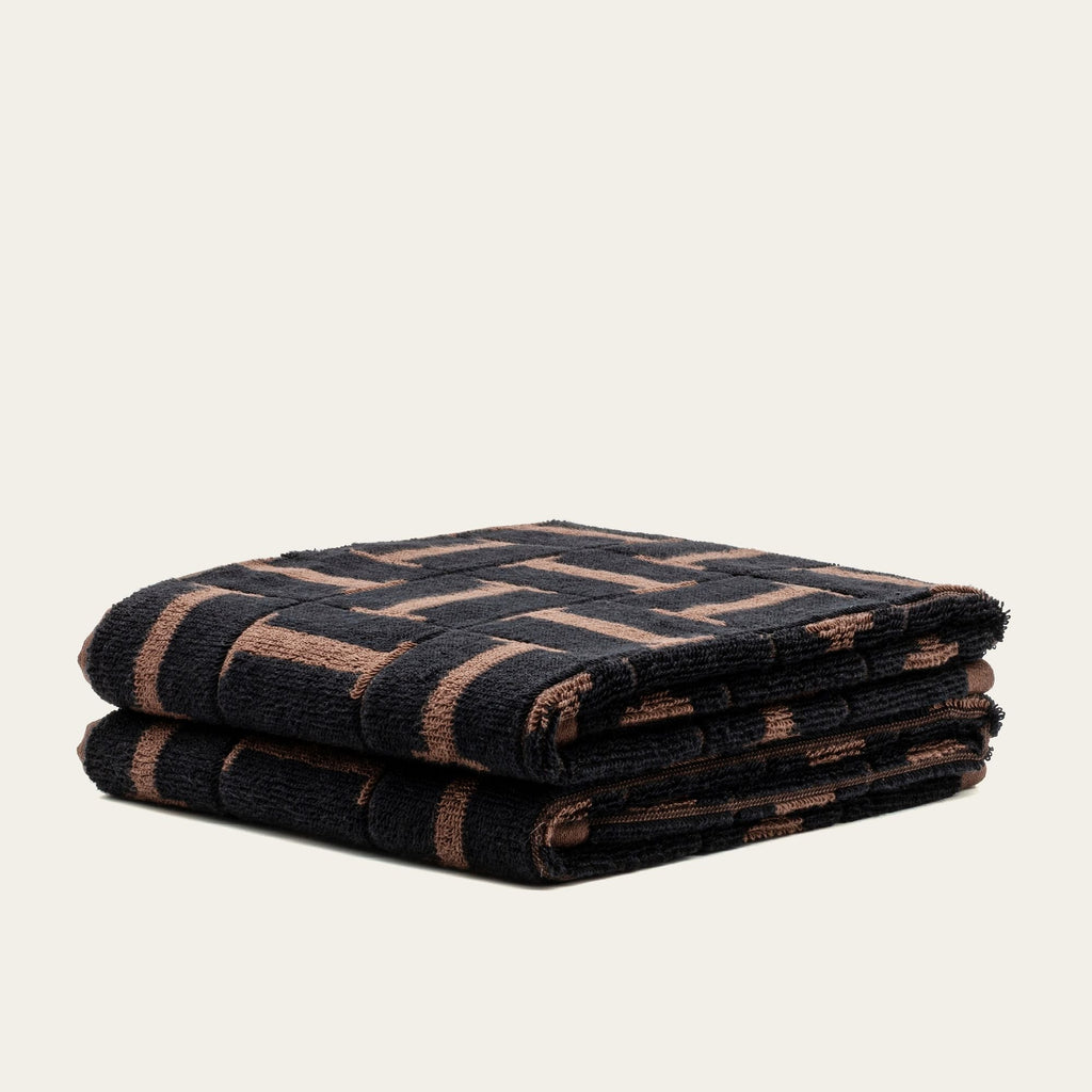 Two folded cotton towels, dark tobacco and black woven geometric pattern