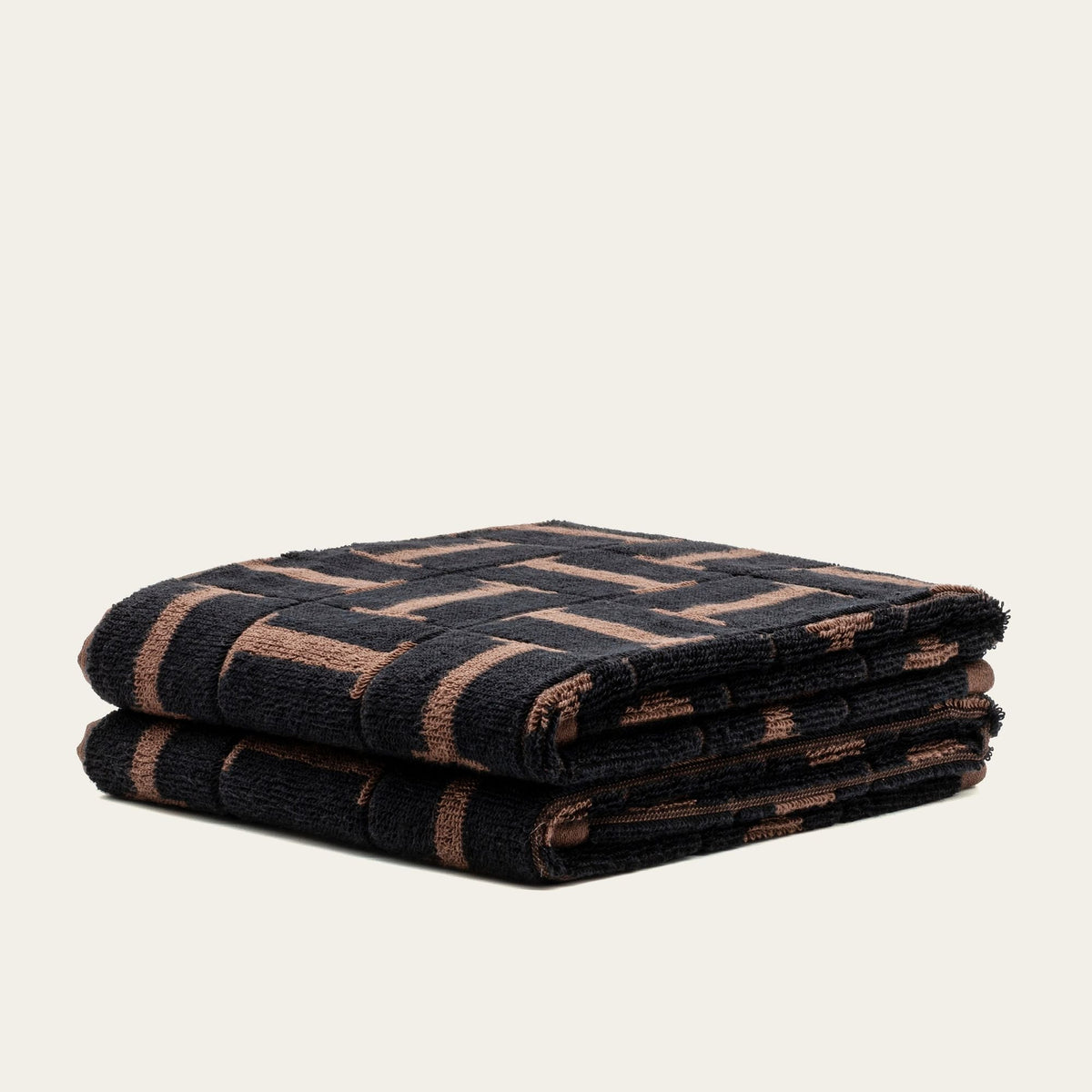 Two folded cotton towels, dark tobacco and black woven geometric pattern