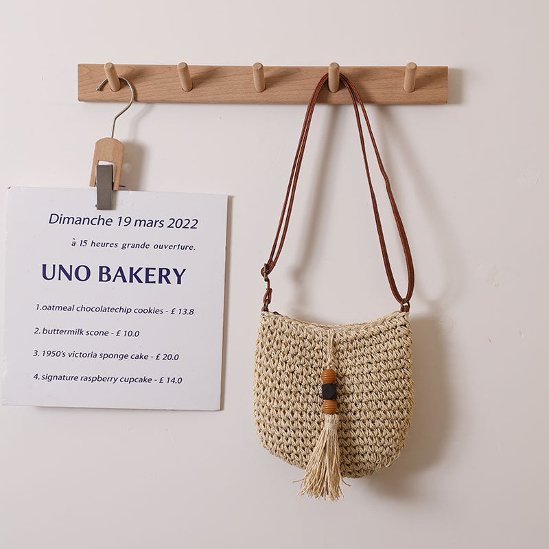 Woven straw crossbody bag with wooden beads, tassel fringe, adjustable leather strap.