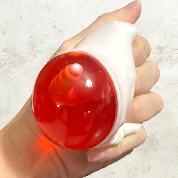 Hand holding white squeezable skull squish toy with glowing red light dome