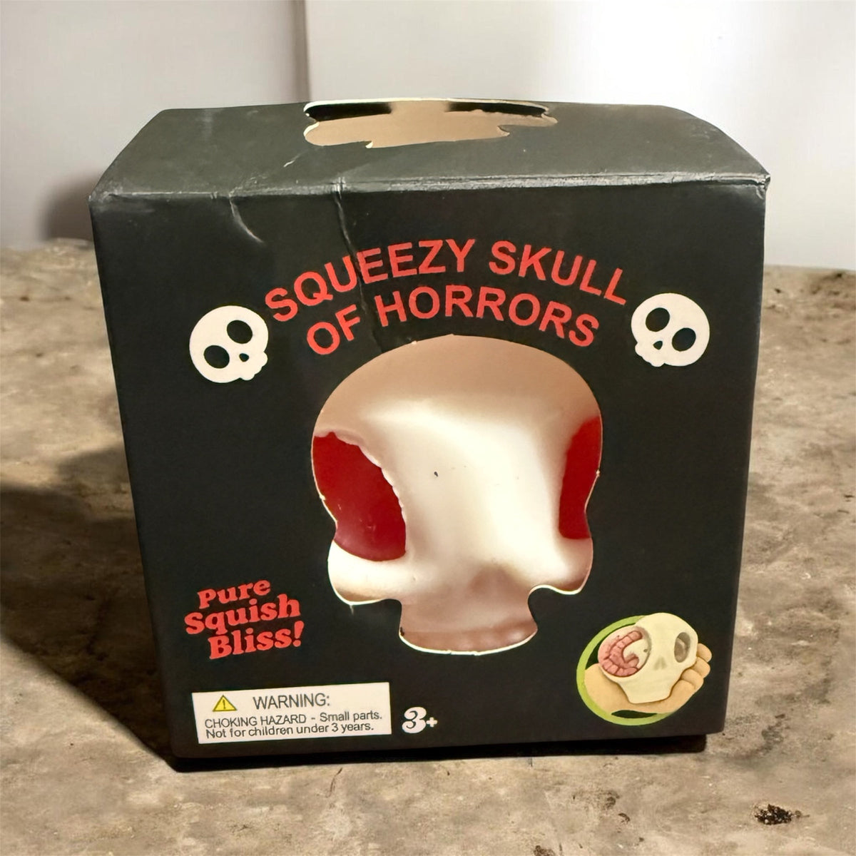 Squeezable skull squish toy black box with red text and skull face window
