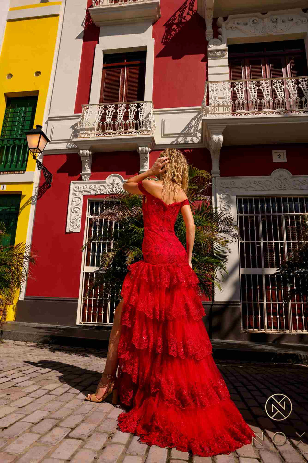 Red off-shoulder corset dress with tiered ruffles and flowing long skirt, slit.