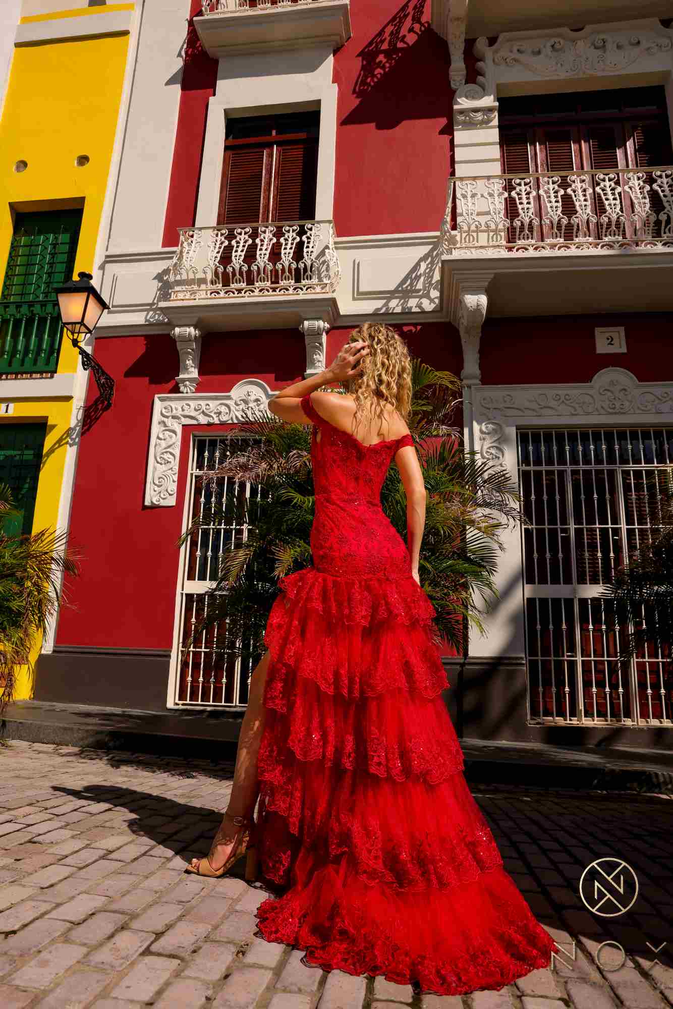 Red off-shoulder corset dress with tiered ruffles and flowing long skirt, slit.