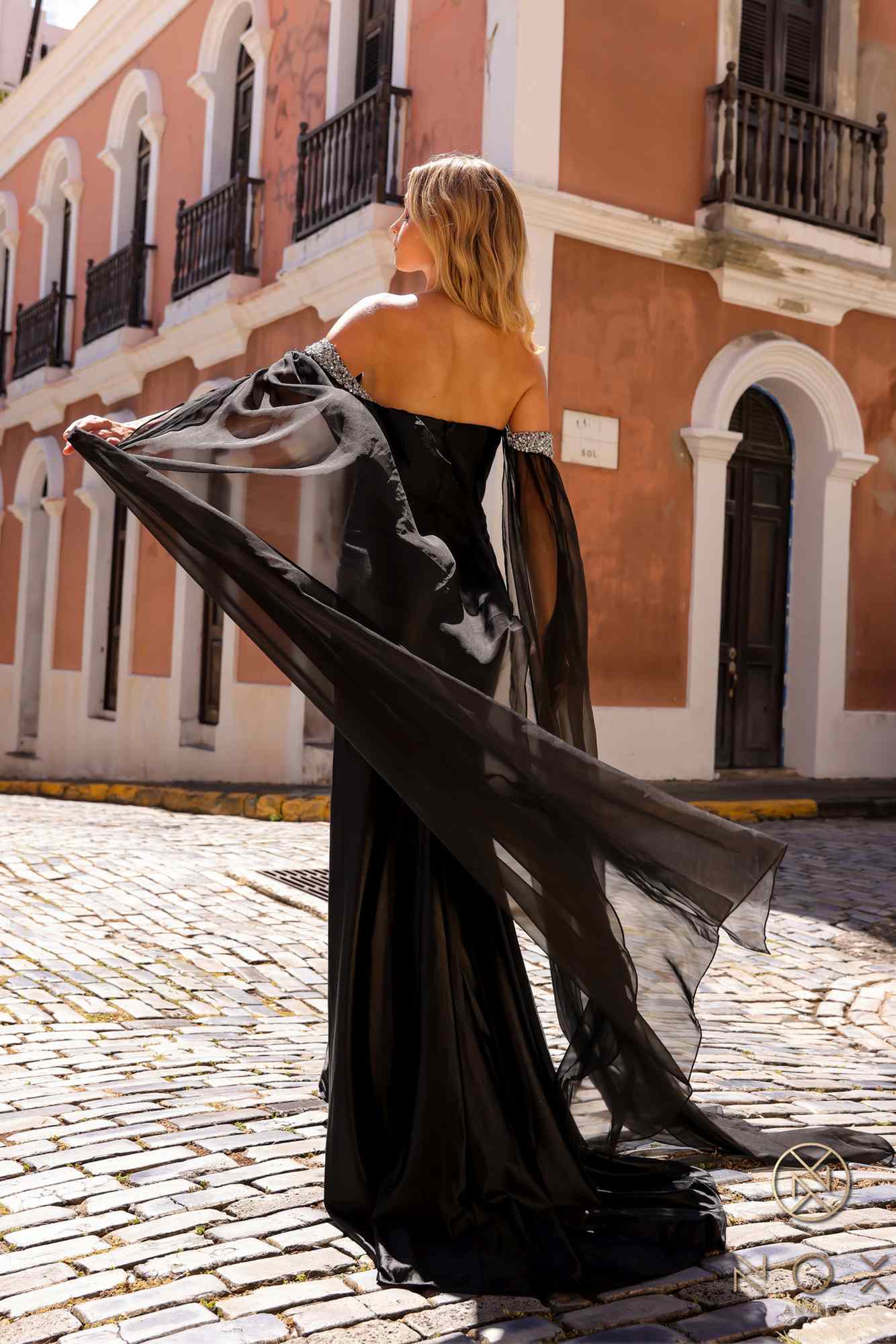 Black satin formal gown, open-back with flowing cape sleeves and thigh slit