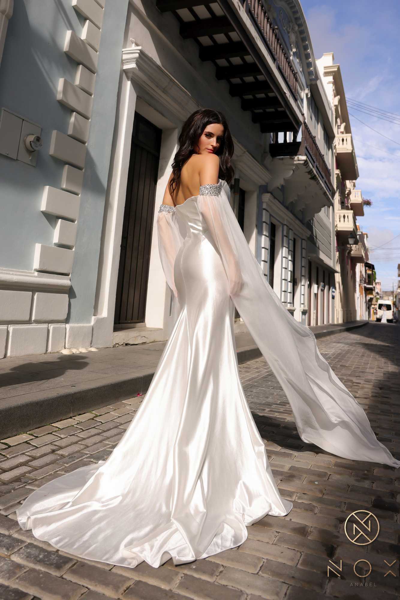 White satin formal gown with cape sleeves, open-back look, and long drape