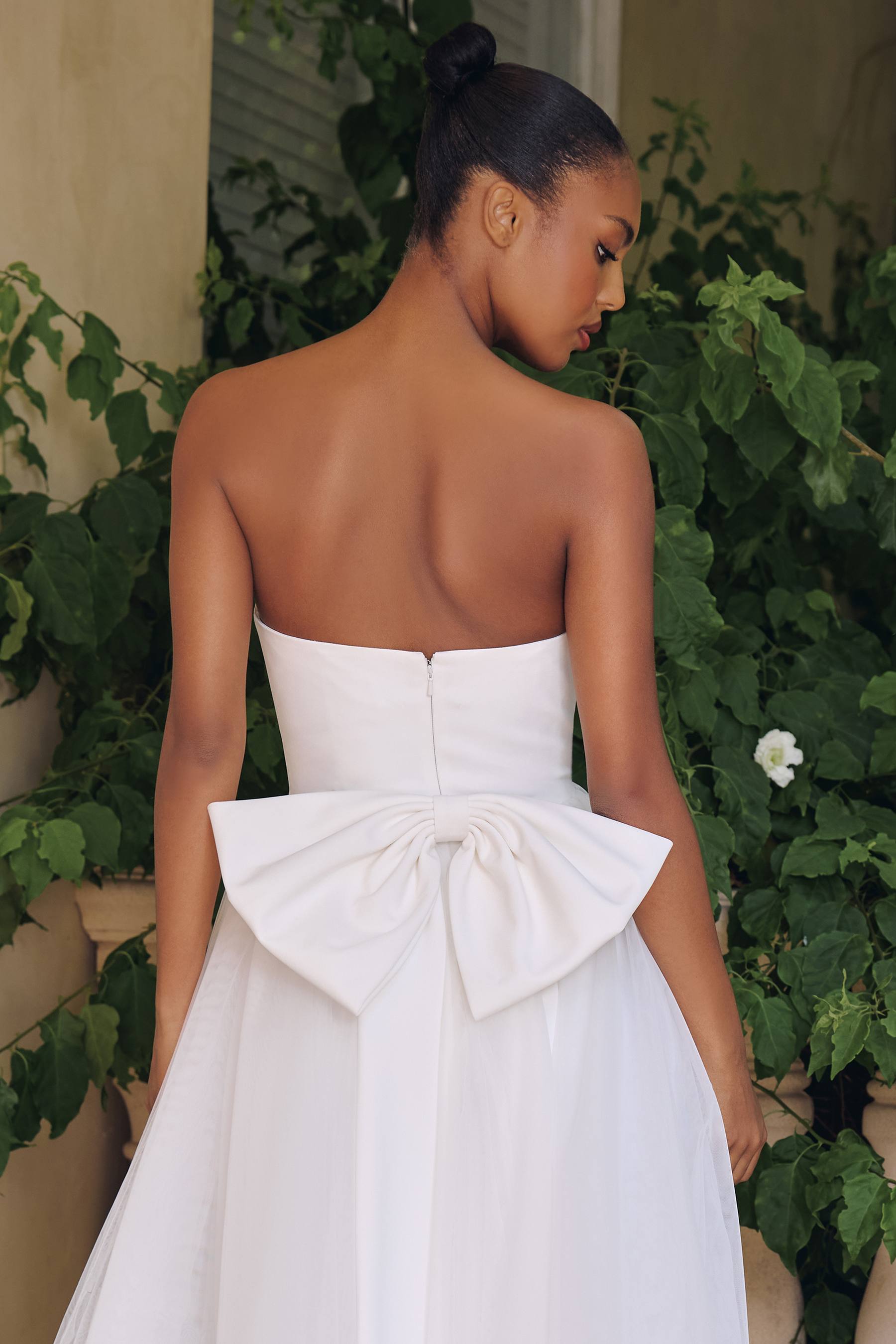 Off-white strapless bridal gown with open back and bow at waist, layered tulle skirt