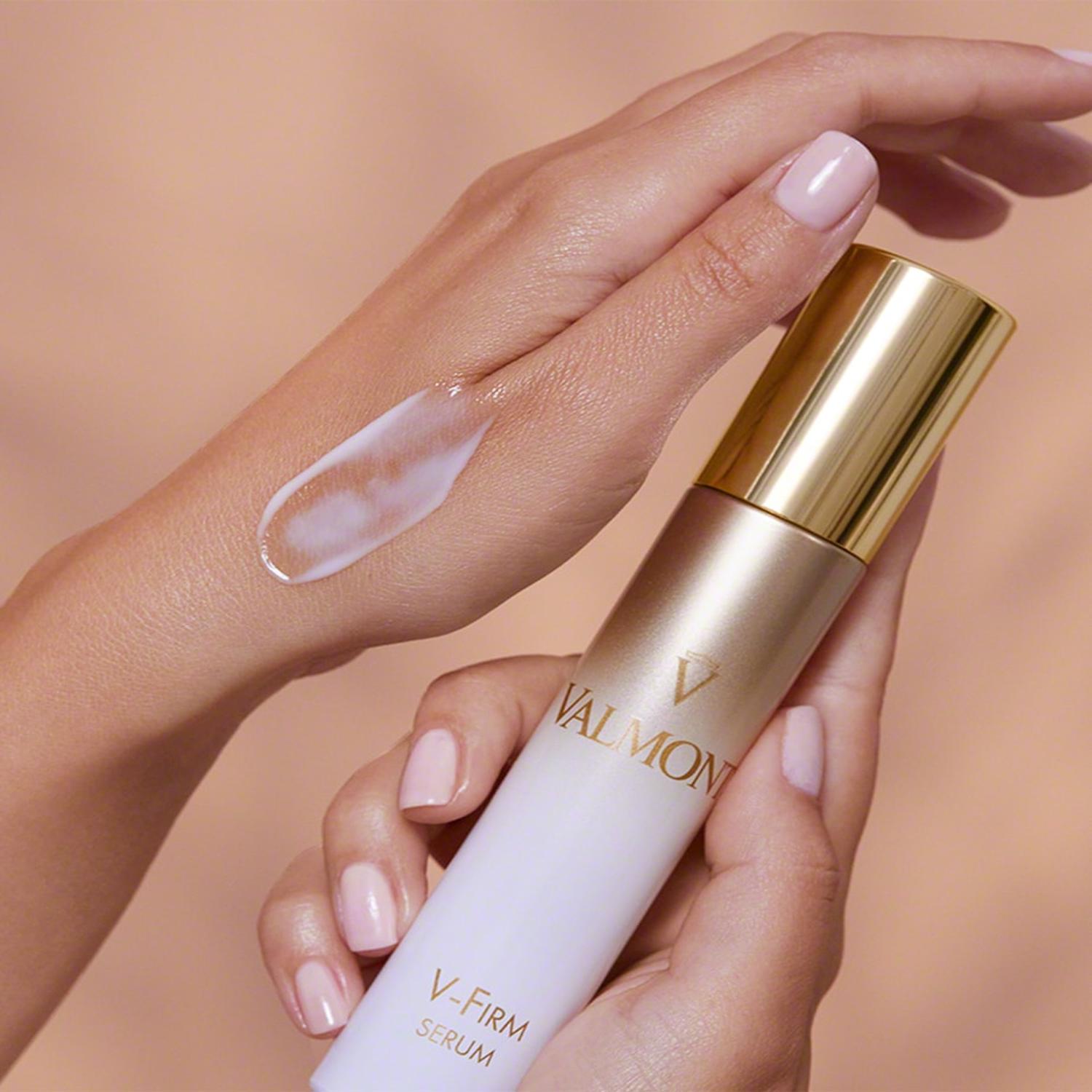 Valmont V-Firm serum bottle with applicator in hands, clear gel on back of hand