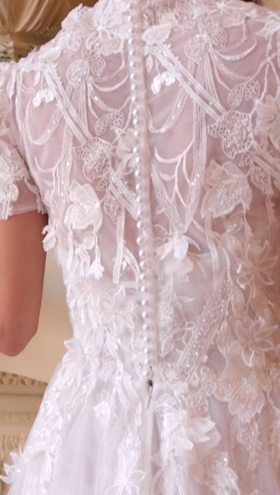 Off-white lace wedding dress bodice detail with floral appliques and pearl trim