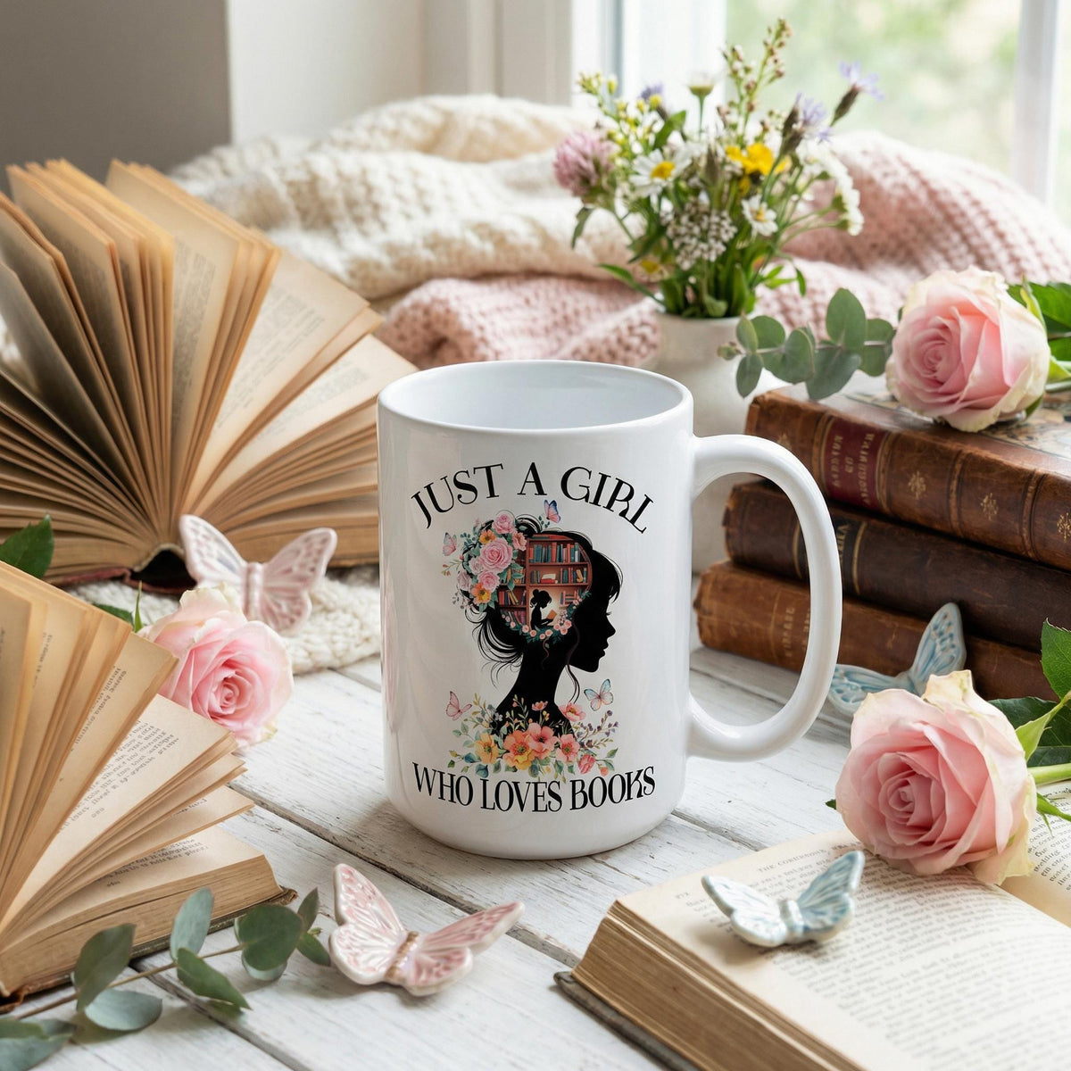 Ceramic coffee mug on books and flowers, featuring “JUST A GIRL WHO LOVES BOOKS” graphic.