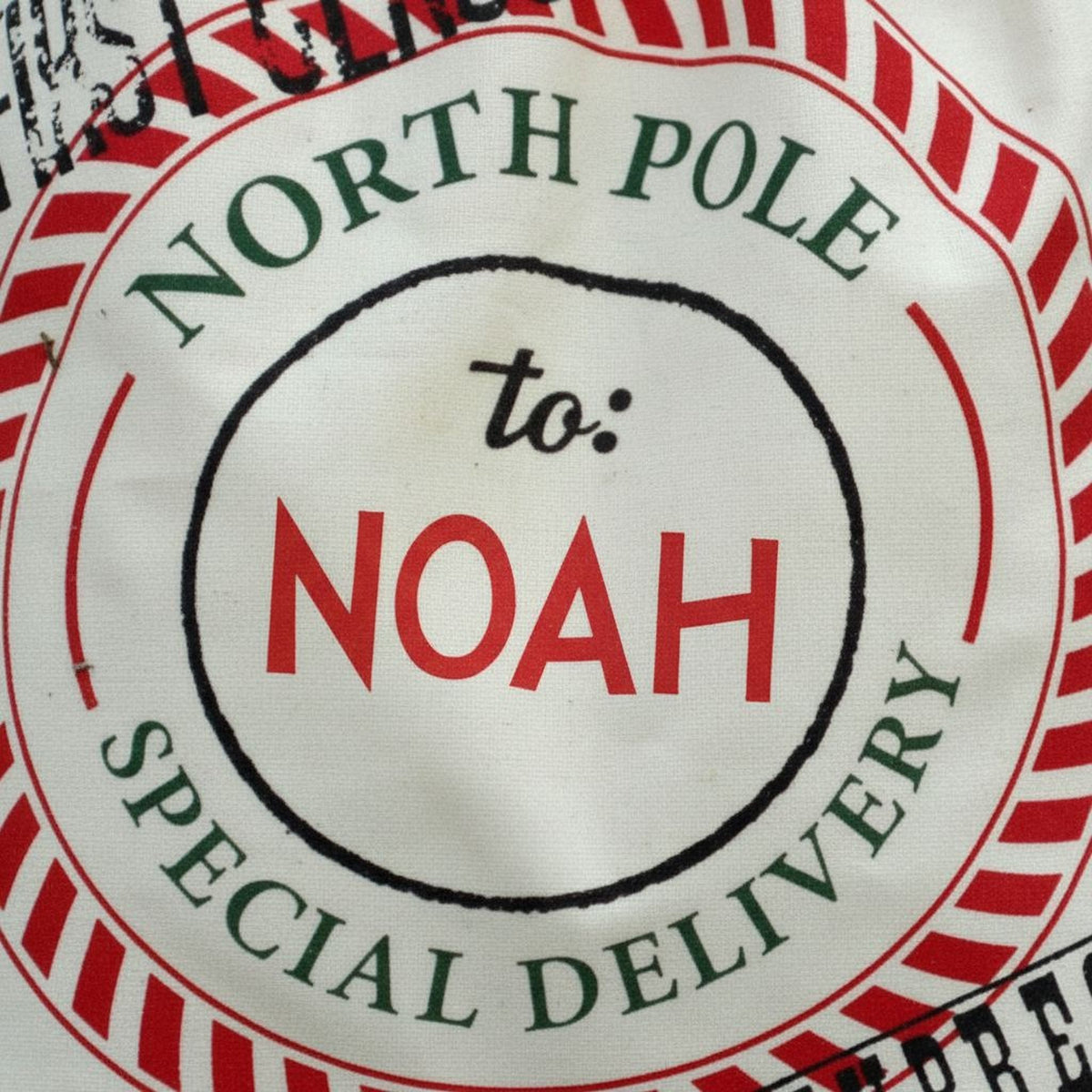 Close-up of North Pole seal on cream Santa bag with 'to: NOAH' text.