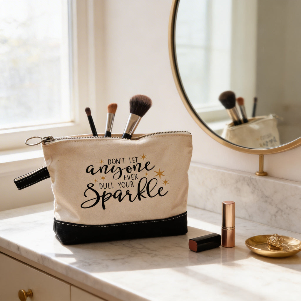Beige canvas makeup pouch with black bottom, zipper pull, and 'anyone ... Sparkle' message.