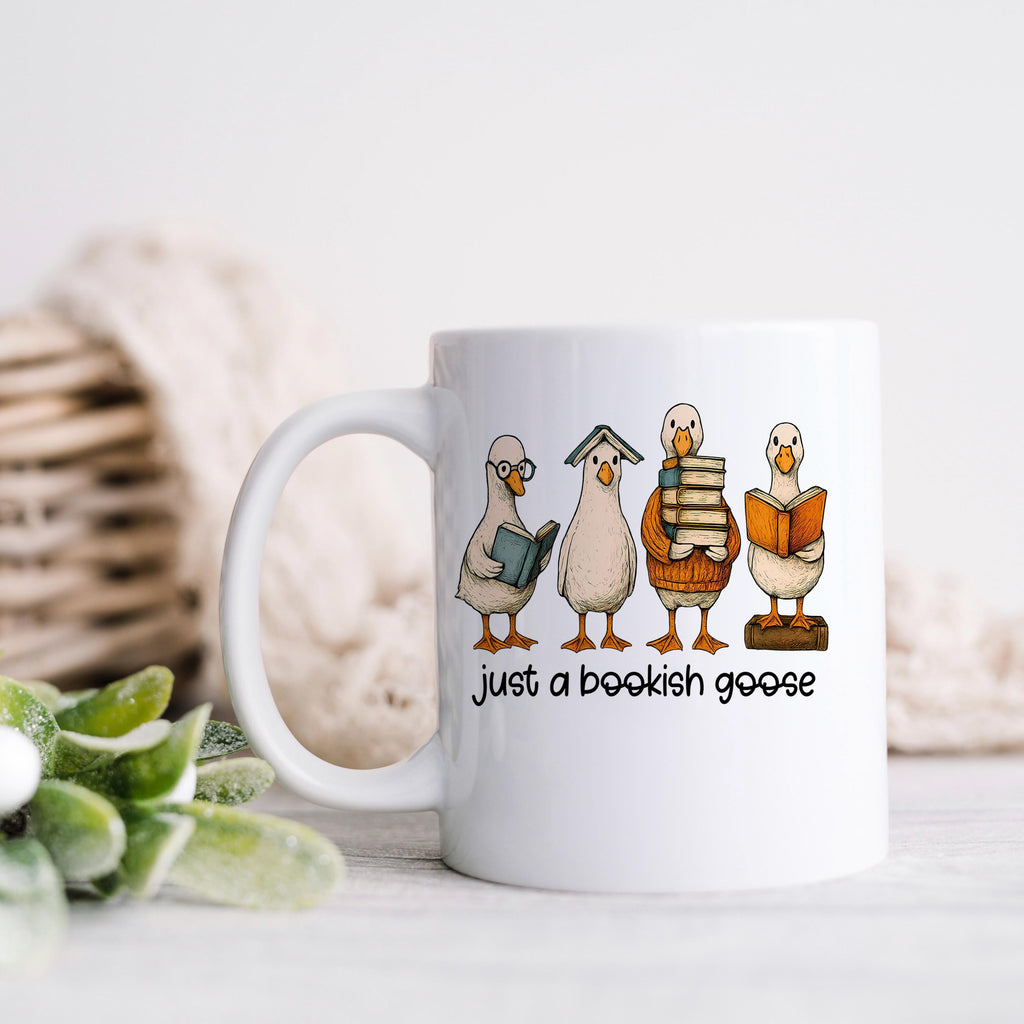 White coffee mug with bookish goose cartoon scene and "just a bookish goose"