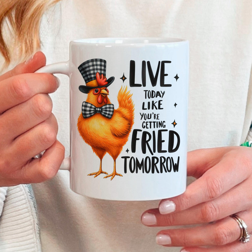 Hand holding white ceramic mug with orange cartoon chicken and LIVE…FRIED TOMORROW text