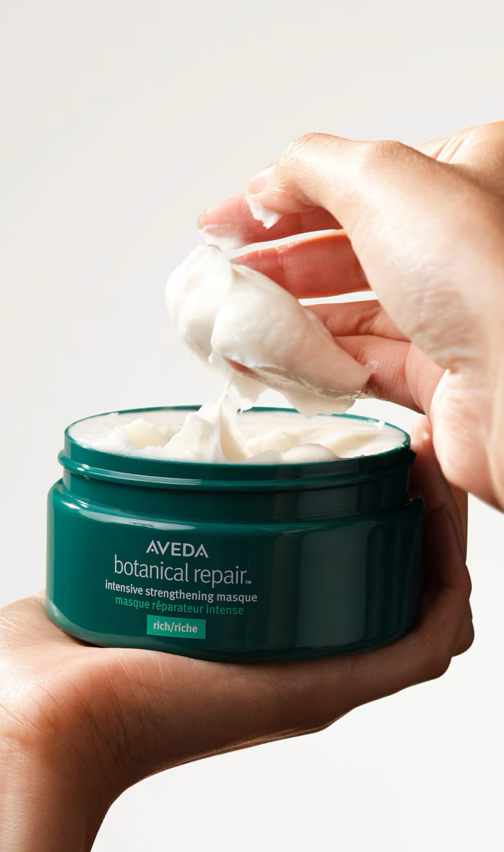 Aveda hair masque jar held as creamy white product is scooped