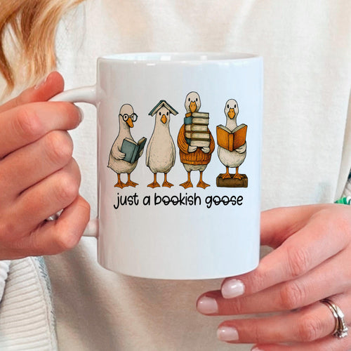 White ceramic coffee mug with four bookish goose characters and the phrase "just a bookish goose"