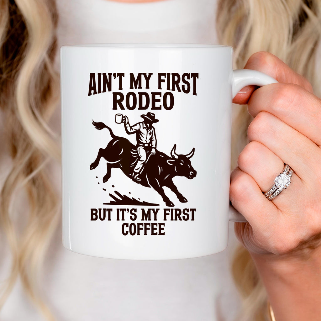 White ceramic coffee mug in hand, featuring rodeo quote and bull rider graphic.