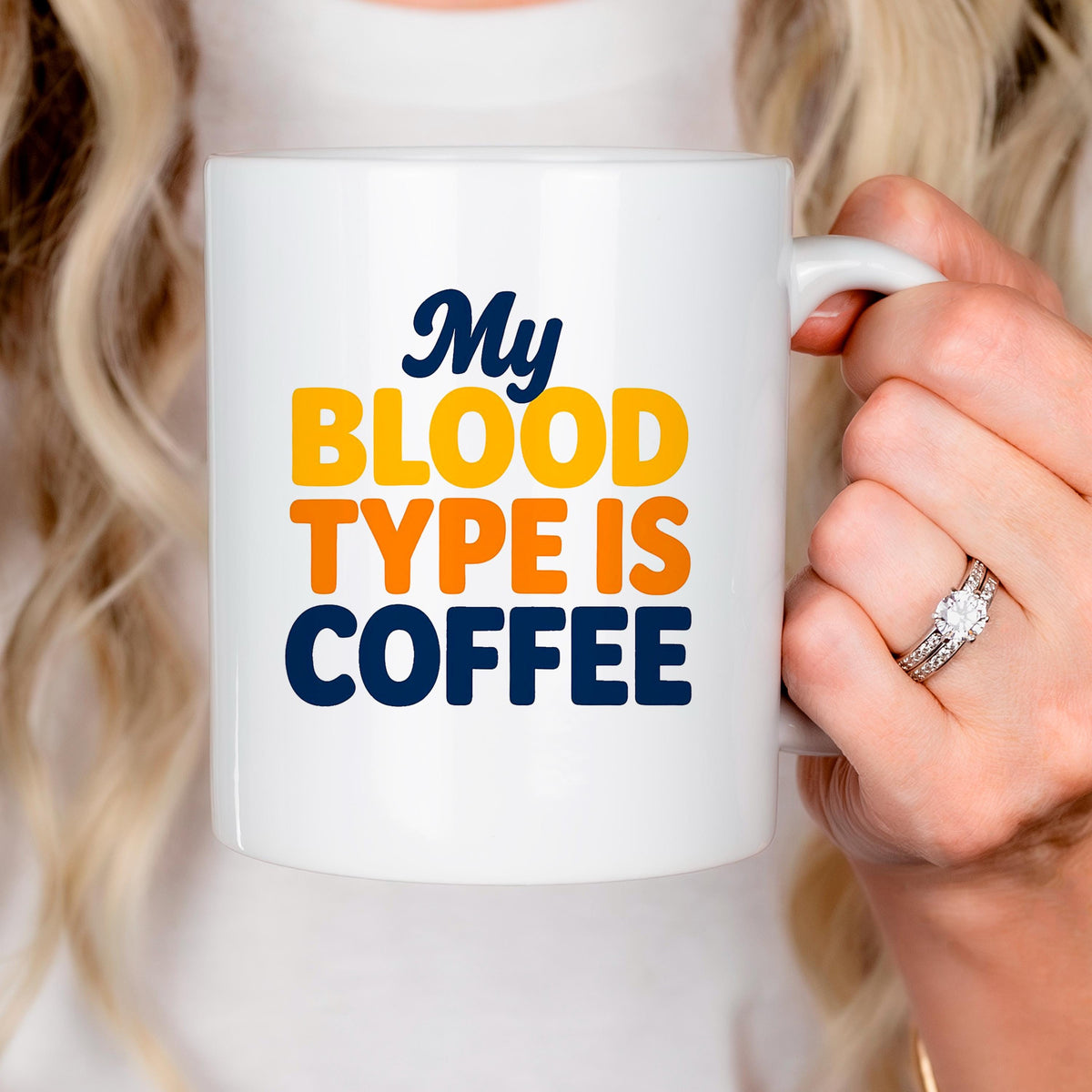 White ceramic coffee mug being held near face, “My BLOOD TYPE IS COFFEE” printed.