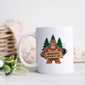 White ceramic coffee mug with Bigfoot graphic holding sign and steaming cup.
