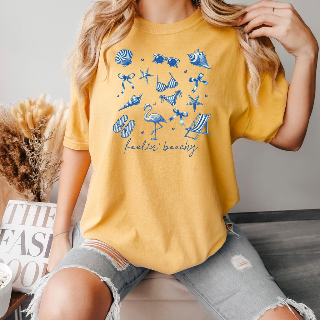 Mustard beach graphic unisex tee with blue coastal icon set and “feelin’ beachy” print