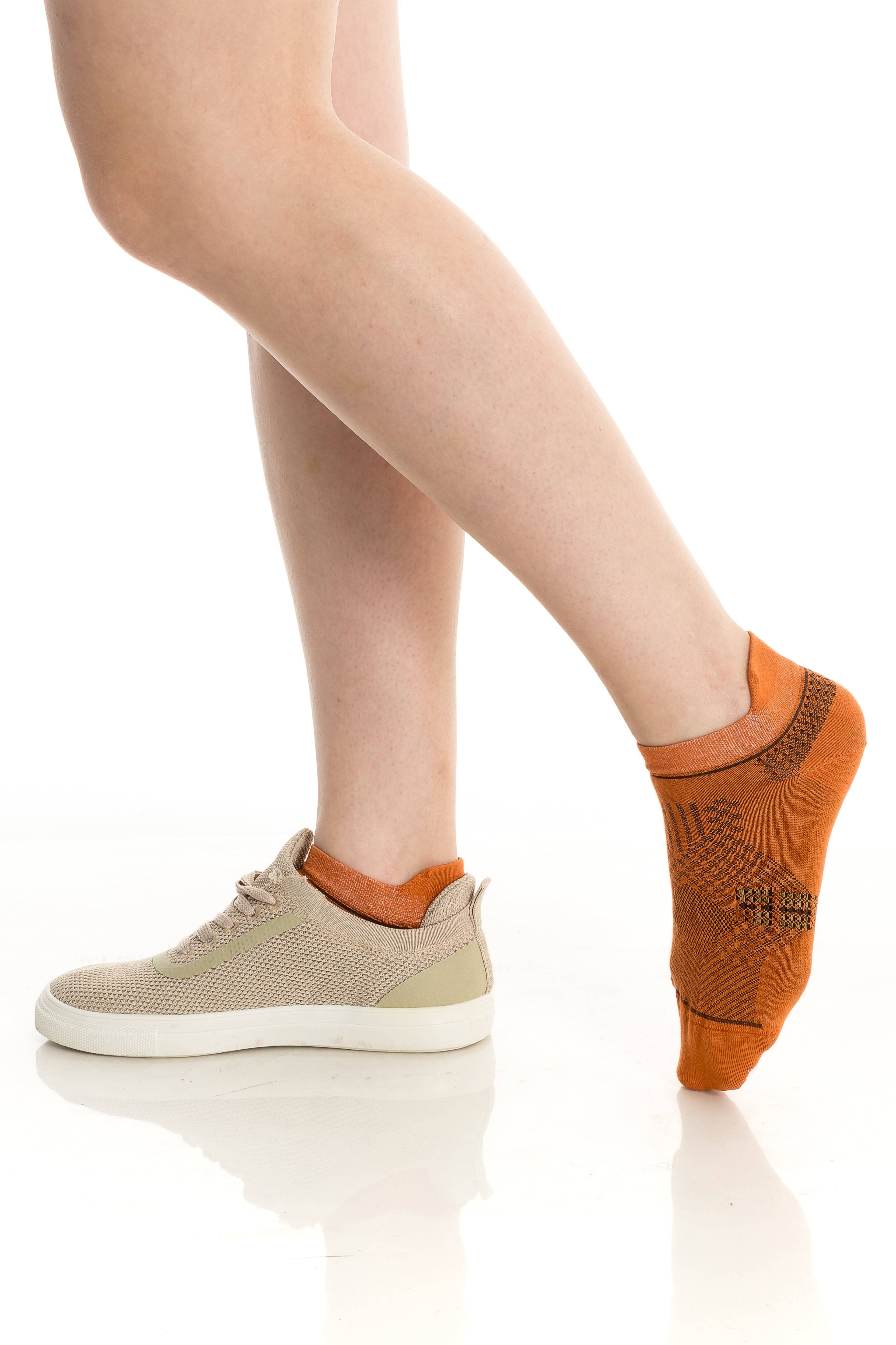 Orange ankle socks with dark geometric knit pattern, shown on an ankle