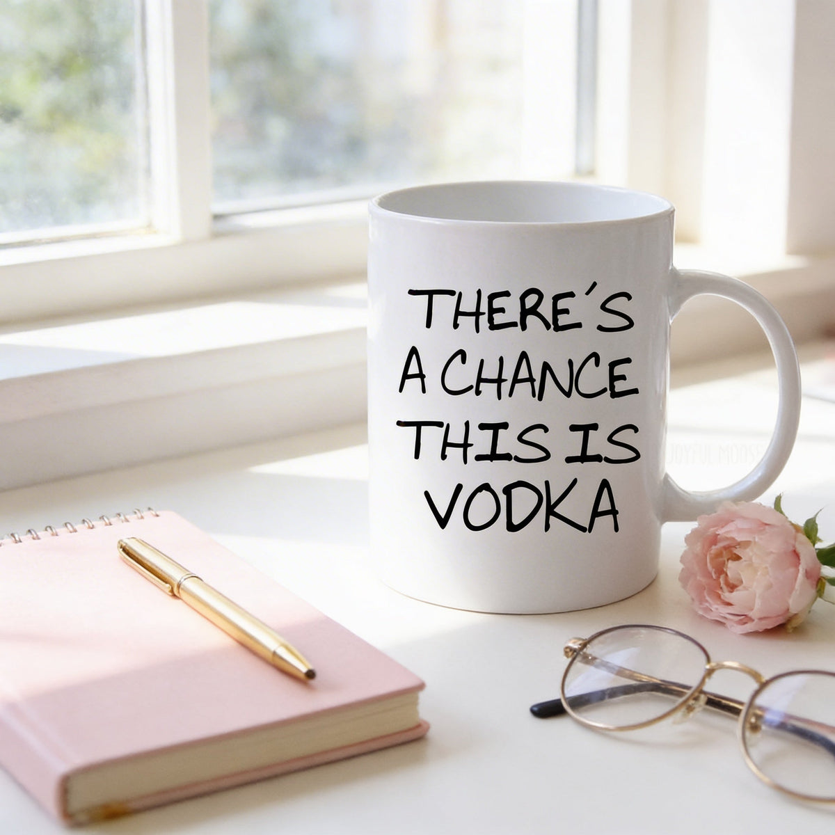 White coffee mug with 'THERE'S A CHANCE THIS IS VODKA' on table near flower