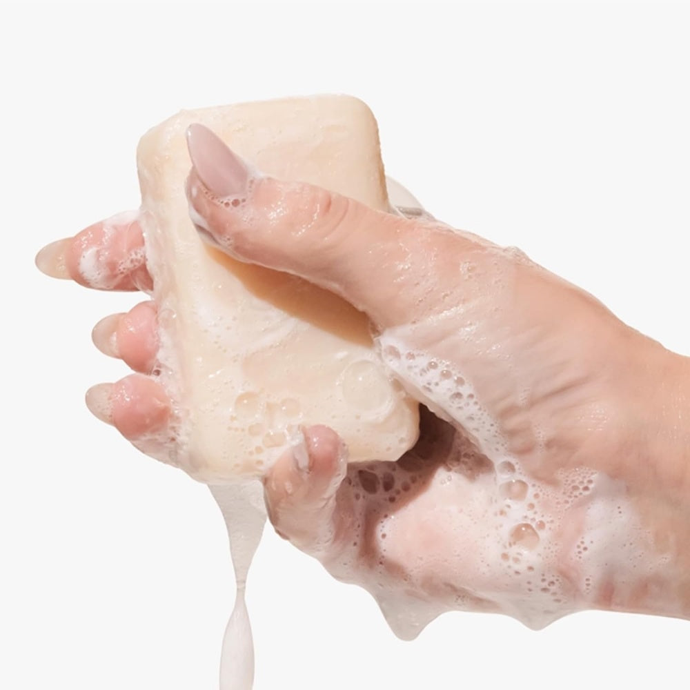 Hands holding a goat-milk soap bar with creamy lather