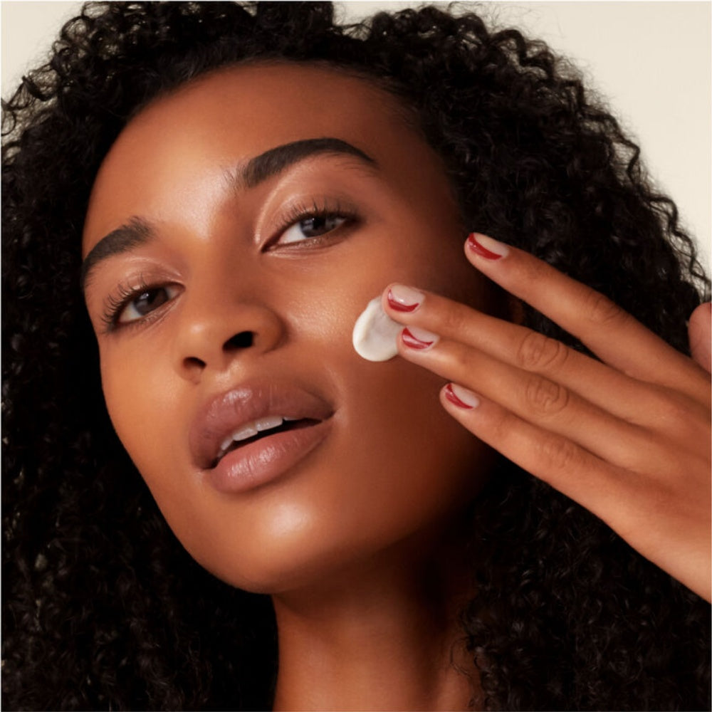 Shiseido Benefiance cream applied on fingertip near face, pink jar visible