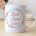 White coffee mug with pink floral wreath and "Best Mom Ever" lettering, side handle