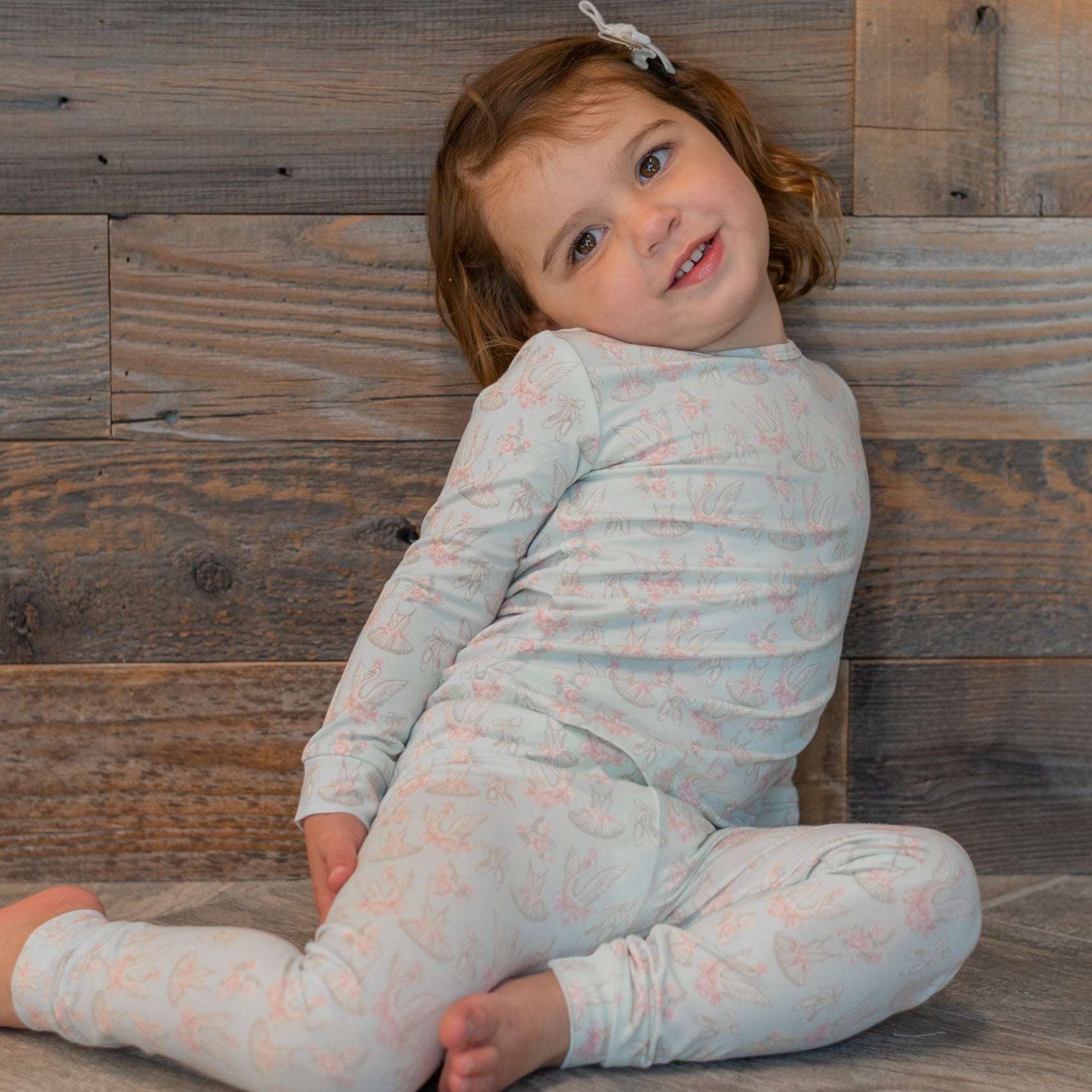 Girls' long-sleeve pajama set with pastel swan ballet print, worn while seated