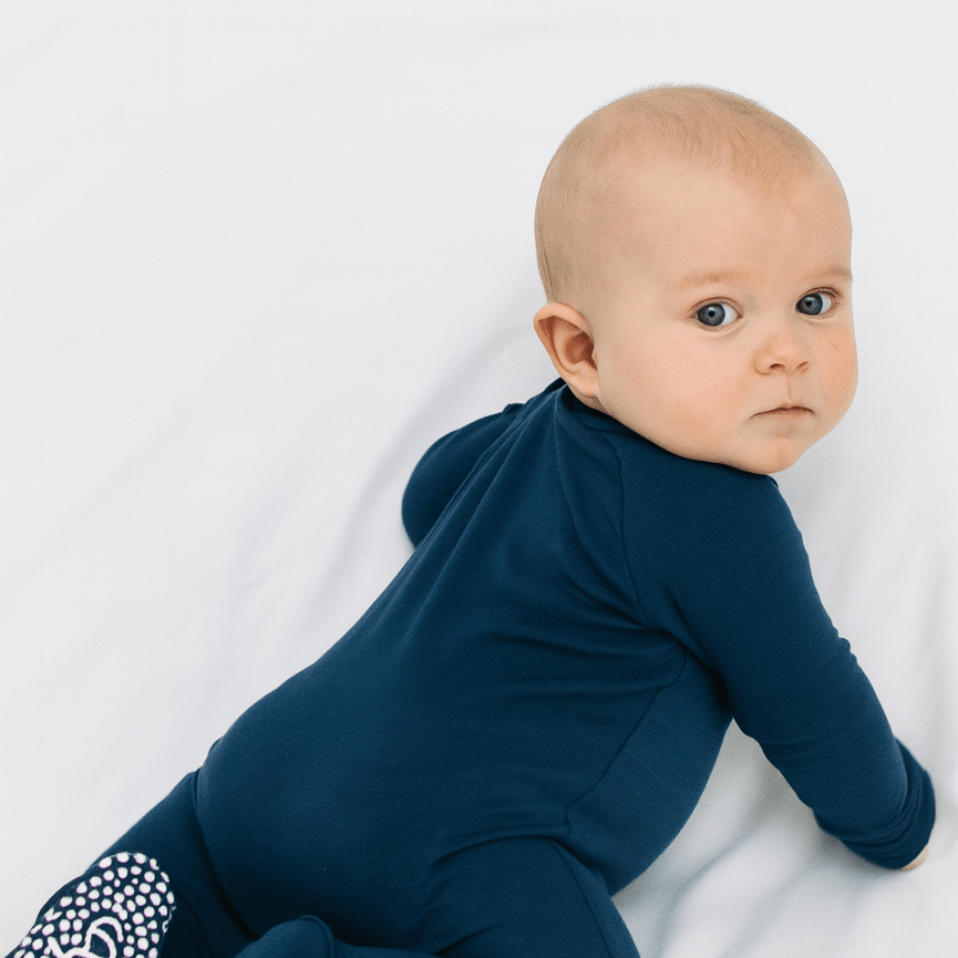 Baby in dark blue long-sleeve zipper footie, standing turned to the side